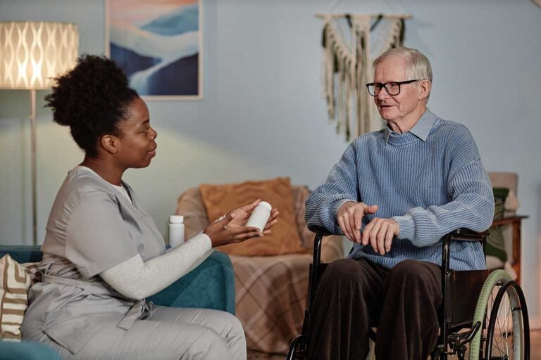 Assisted living staff member talking with an elderly resident at a dining table.