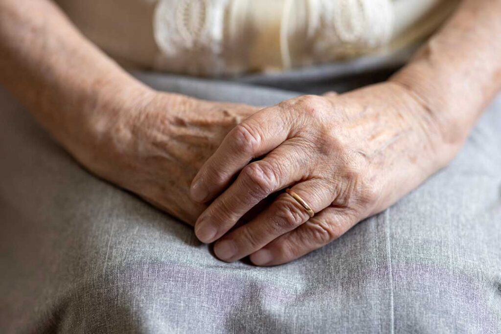 An older woman arranges family photos in her assisted living room while a relative sits nearby.